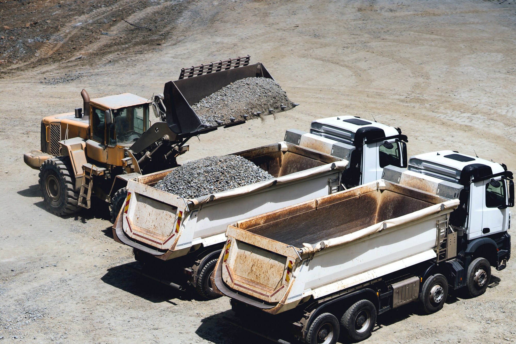Dumper trucks being loaded on ore mine, works at open pit mine. Wheel loader loading trucks